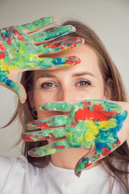 Brownhaired woman shows hands in bright paints posing