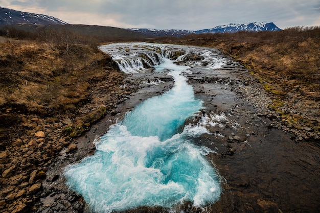 Photo bruarfoss waterfall in iceland with vibrant blue waters and a rugged landscape