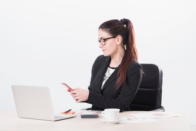 Bruentte woman sitting in the office with phone and notebook isolated on white