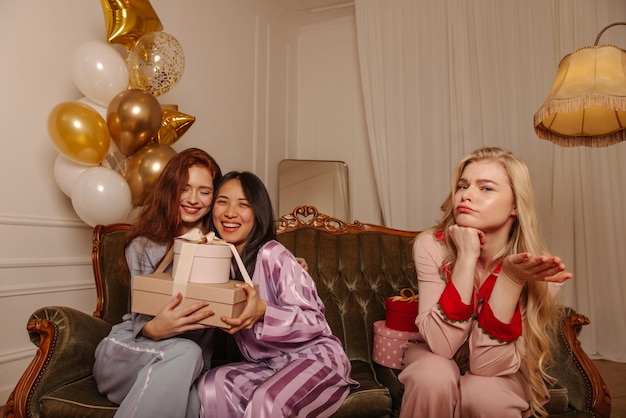 Brunette asian woman and caucasian redhead rejoice at received gifts while sitting near indignant blonde Relax lifestyle concept