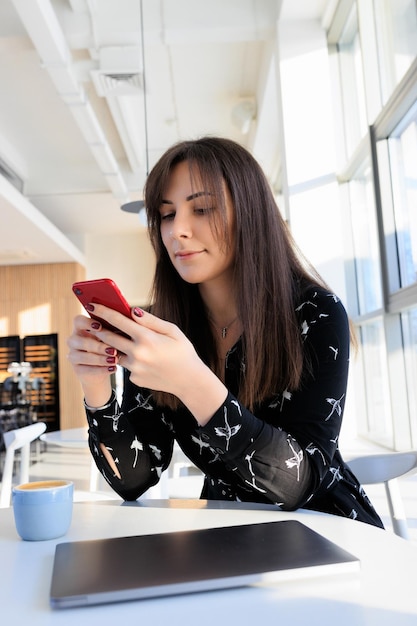 Brunette in a black dress typing on her phone in a cafe