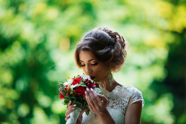 Brunette bride in a wedding dress and a bouquet at sunset in the park