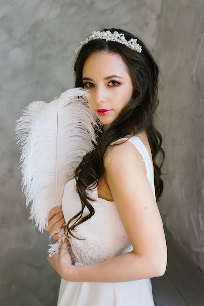 Brunette bride with tiara and professional makeup holding a white ostrich feather 