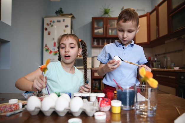 Brunette brother and sister decorate Easter eggs sitting at the table at home in the kitchen