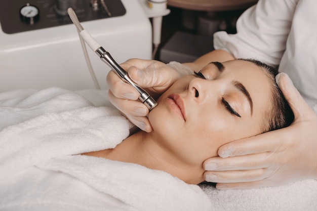 Brunette caucasian woman having a spa procedure for the skin of her face done with an apparatus by a spa worker