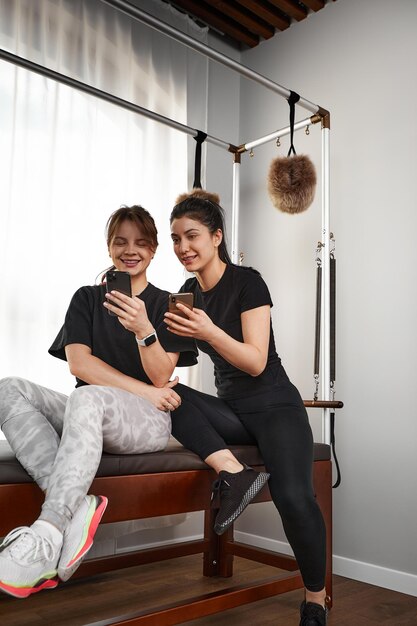 Brunette caucasian woman personal trainer during a workout session on pilates reformer bed equipment with an attractive client in light medical office Healthy lifestyle rehabilitation concept