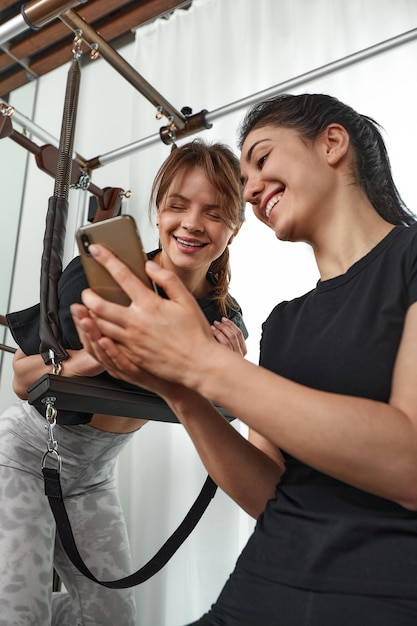 Brunette caucasian woman personal trainer during a workout session on pilates reformer bed equipment with an attractive client in light medical office Healthy lifestyle rehabilitation concept