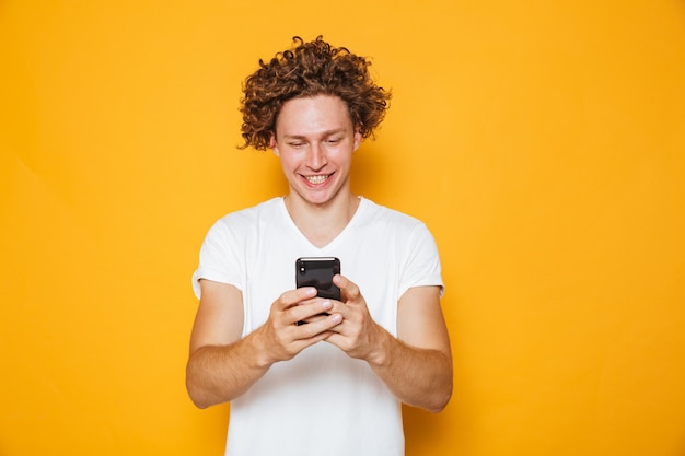 Photo brunette curly man in casual white t-shirt holding and using mobile phone