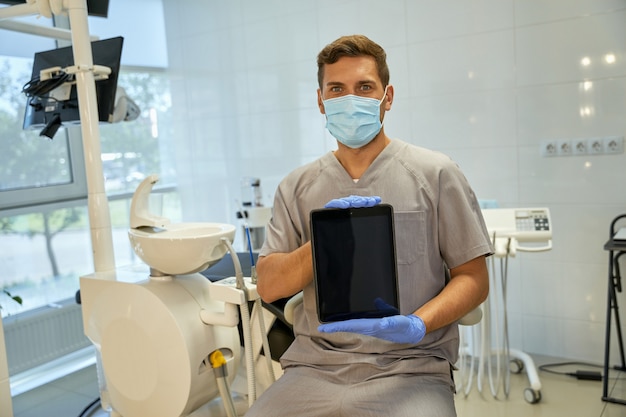 Brunette dentist posing at his office with a tablet