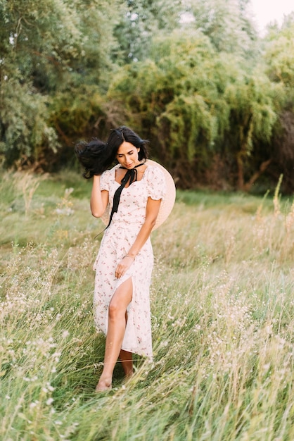 brunette in an elegant summer outfit and straw hat in the rays of sun on nature walk