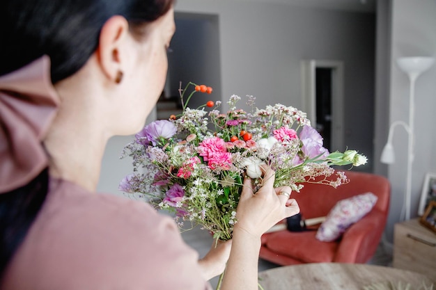 A brunette european young woman florist makes a bouquet of flowers and herbs in her workshop