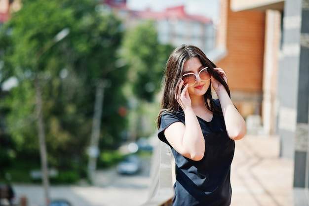 Brunette girl at black dress sunglasses posing at street of city