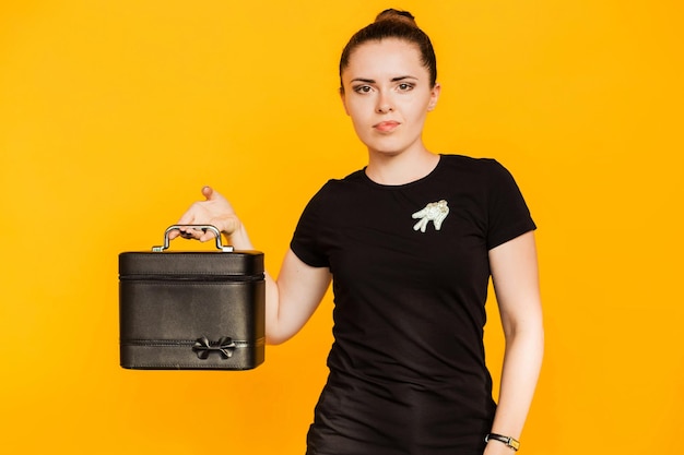 A brunette girl in a black Tshirt demonstrates a black case for beauty masters on a yellow background