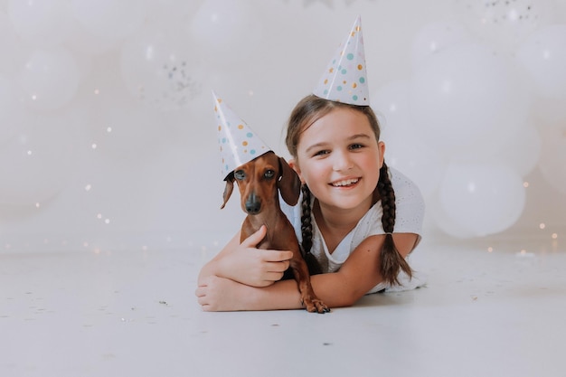 brunette girl and her favorite dog dachshund in festive hats lie on the floor in front of the camera