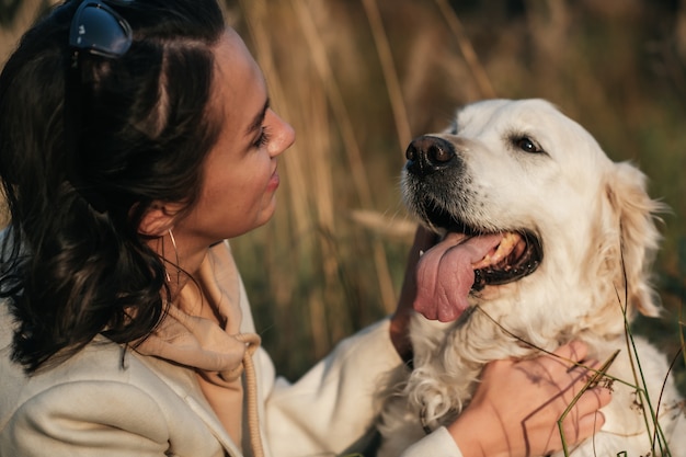 brunette girl hugging white golden retriever in the field