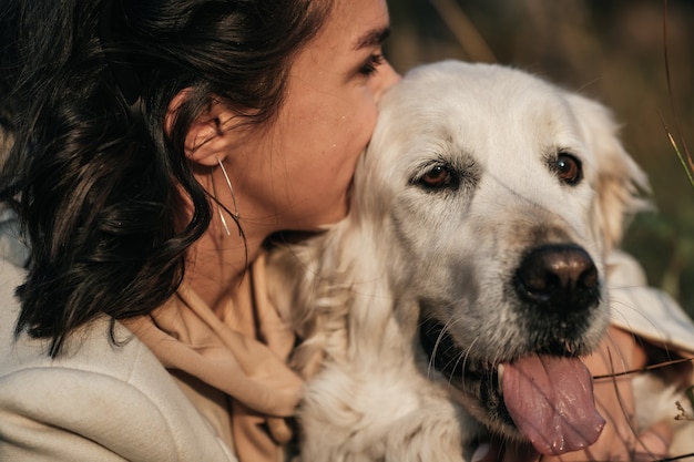 brunette girl hugging white golden retriever in the field