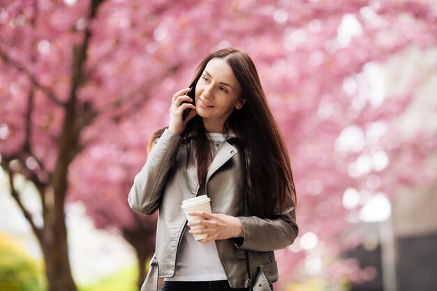 Brunette girl in jacket and jeans in the spring outdoors in the city  flowering sakura trees posing