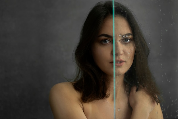 Brunette girl in the shower. Drops of water on the shower screen. Portrait