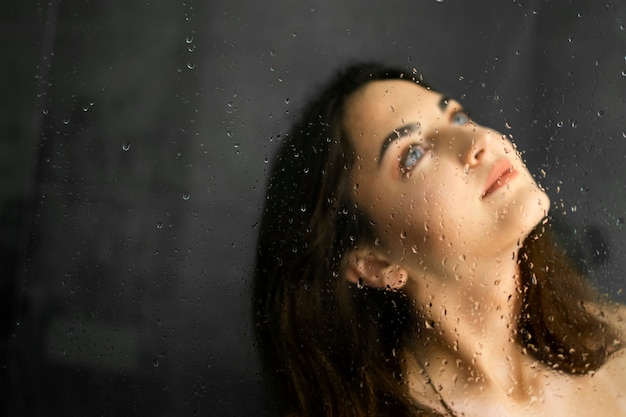 Brunette girl in the shower. Drops of water on the shower screen. Portrait