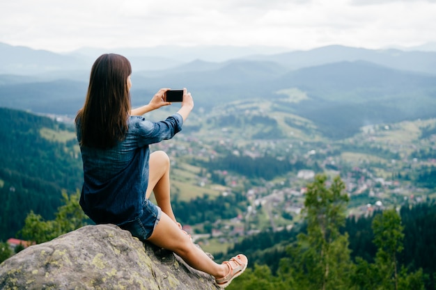 Brunette girl taking selfie with smartphone high in the mountains. 