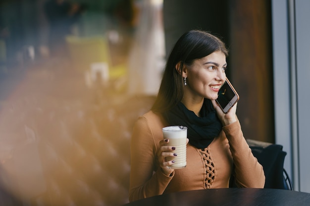 brunette girl using her phone while drinking coffee at a restaurant