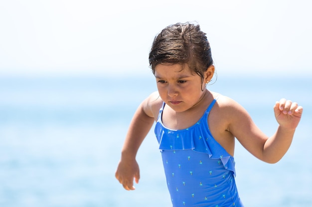 Brunette girl wearing a swimsuit on the beach running with the sky in the background Concept of beach vacation sun protection sea lifestyle and relaxation