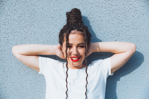 A brunette girl with dreadlocks and red lipstick in a denim suit is standing near a blue wall generation z