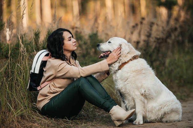 brunette girl with white golden retriever dog on the forest path