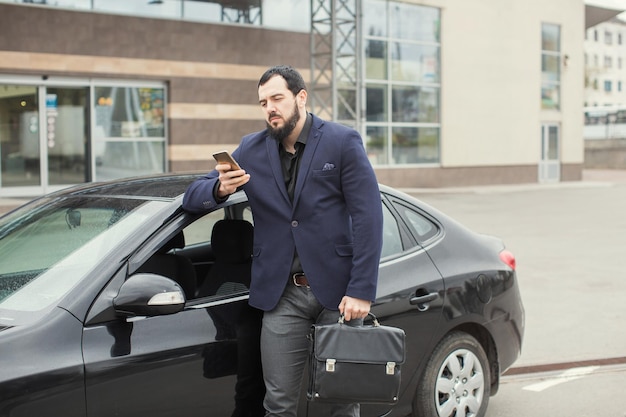 A brunette guy with a beard near a black car