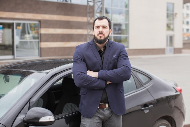 A brunette guy with a beard near a black car