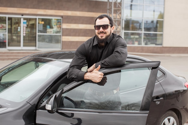 A brunette guy with a beard near a black car