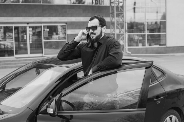 A brunette guy with a beard near a black car