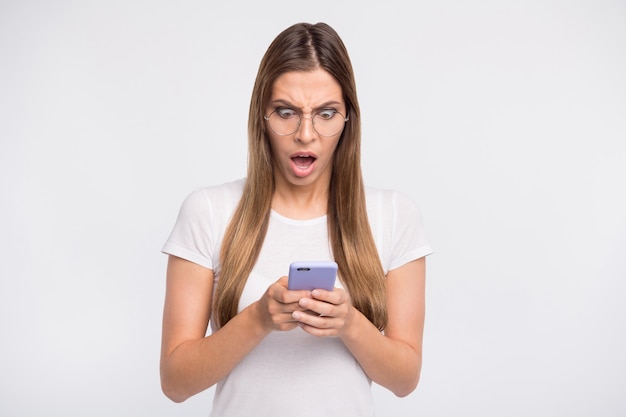 brunette lady with glasses posing against the white wall with her phone