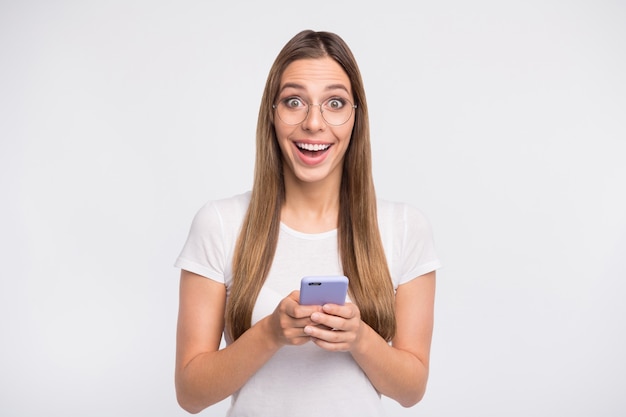 brunette lady with glasses posing against the white wall with her phone