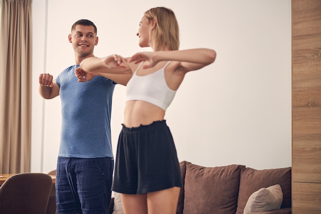  brunette man and cute blond lady exercising at home in cosy atmosphere near sofa