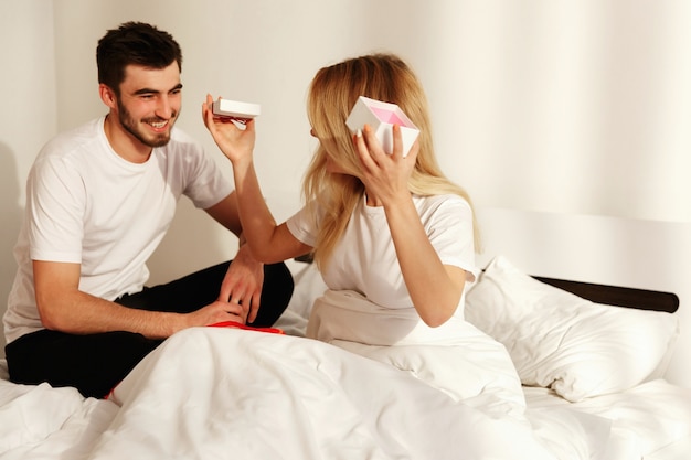 Brunette man gives to his woman a gift while she lies in the bed in the morning 