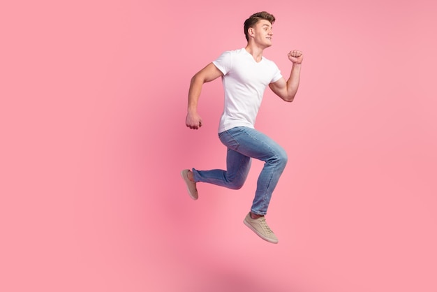 Brunette man in sneakers denim outfit running in air hurrying for discounts for advertising studio shot isolated on pink background