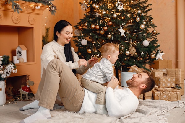 Brunette mother father and little son sitting near Christmas tree and playing