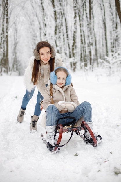 Brunette mother and and her daughter riding a sled in winter forest