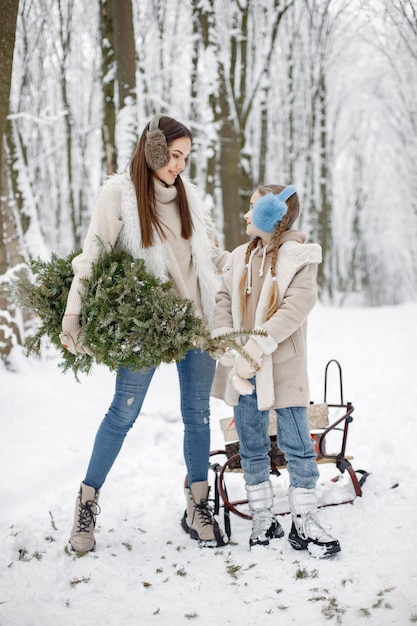 Brunette mother and and her daughter standing near a sled in winter forest