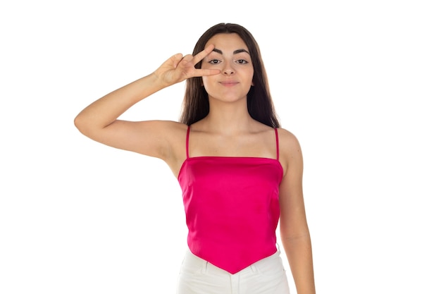 Brunette teenager girl wearing pink top doing peace symbol with fingers over face