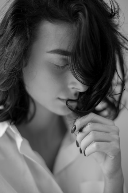 Brunette with curly hair wearing a white shirt posing sitting on the window black and white photo