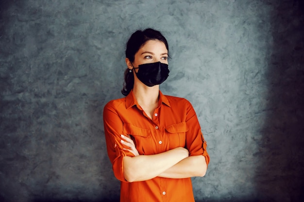 Brunette with face mask standing with arms crossed. You have to believe corona is going to pass.