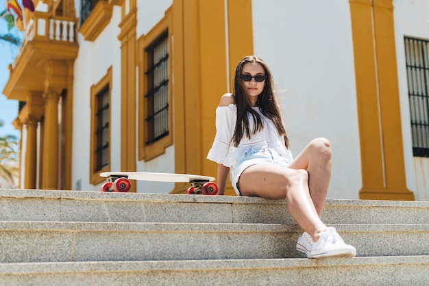 Brunette with long flowing hair sits on the steps of a southern Spanish town nearby stands a skateboard