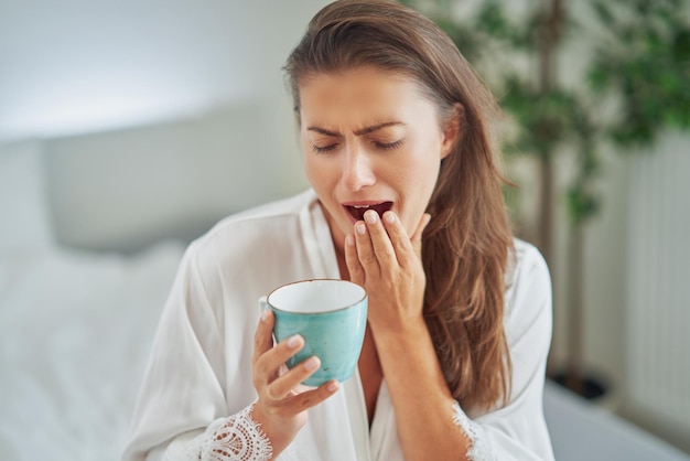 Brunette woman on bad in pajama with mug with coffee or tea