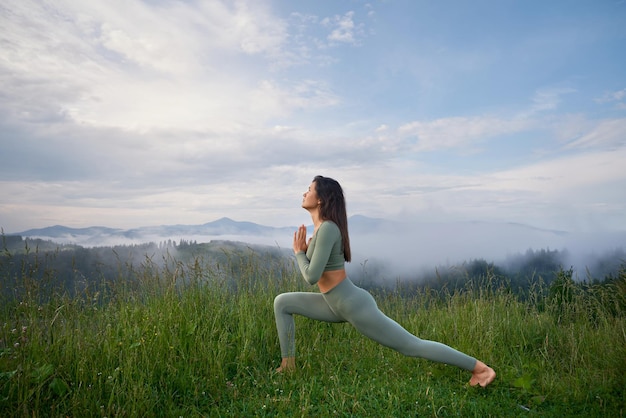 Brunette woman doing pose of warrior in mountains