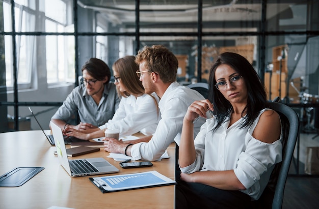 Brunette woman in front of employees. Young business people in formal clothes working in the office.