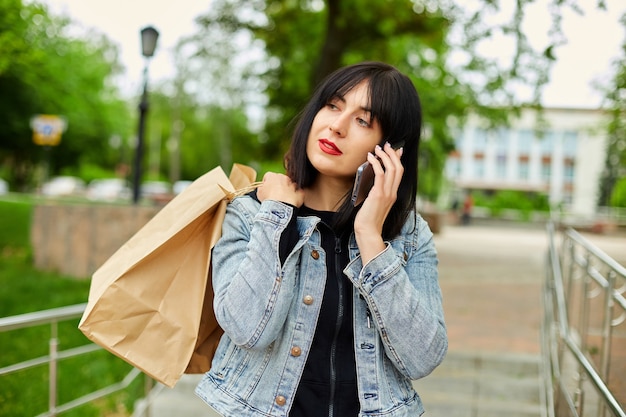 Brunette woman holding paper shopping bags and talking by phone