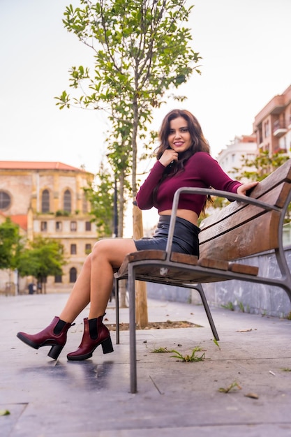 A brunette woman in a leather skirt sitting in the city with a church in the background in autumn