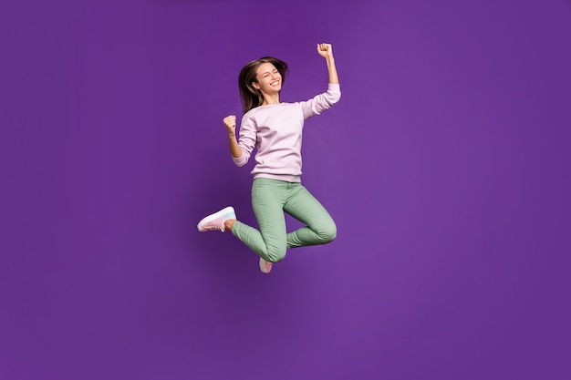 Brunette woman in pastel sweater posing against the purple wall